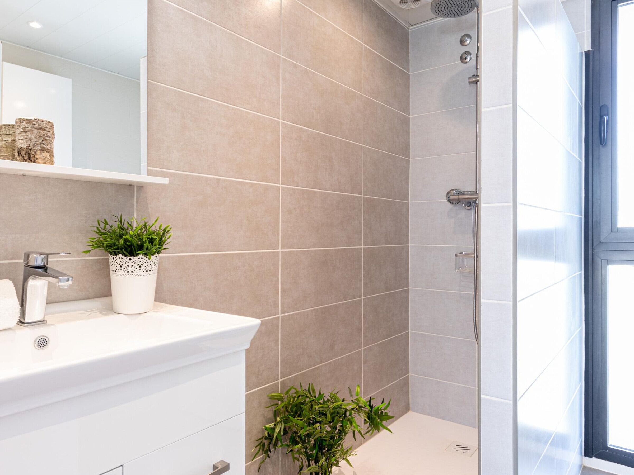 Un baño moderno con un lavamanos blanco, dos plantas en macetas y una zona de ducha.