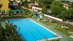 A swimming pool with clear blue water, surrounded by a grassy area with trees and a view of mountains in the background. - Apt 6 People, Parking, Air Con, Stunning View (Sant Pere Pescador)