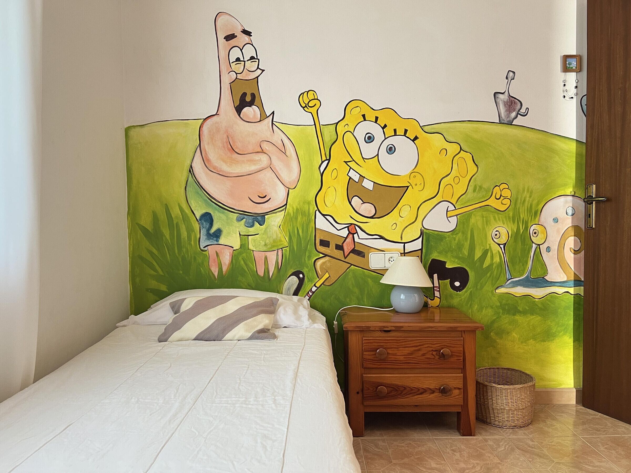 Ein Schlafzimmer mit einem Bett, einem Nachttisch und einer Wandmalerei mit Zeichentrickfiguren.