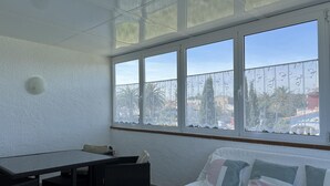 Una habitación con una mesa de comedor, un sofá con cojines y un ventanal con vistas a palmeras y edificios.