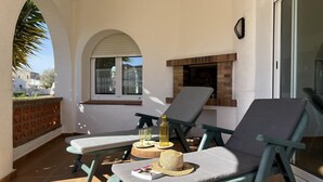 Un balcón con dos sillones de relax, una mesita con una botella y vasos, un libro y un sombrero decorativo.