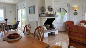 Un comedor con mesa de madera, sillas, chimenea y vistas a través de puertas de cristal.