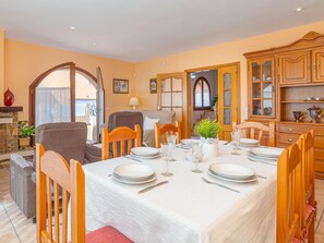 A dining area with a table set for four, wooden chairs, a white tablecloth, and a kitchen area with wooden cabinets.
