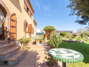 A courtyard with a tiled patio, steps leading to a wooden door, and various potted plants.