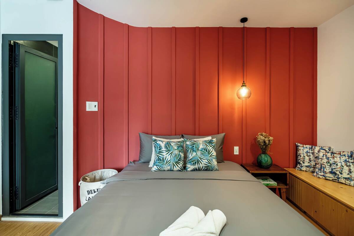 Een moderne slaapkamer met een groot bed, rode accentmuren, een nachtkastje met een vaas en een hanglamp.