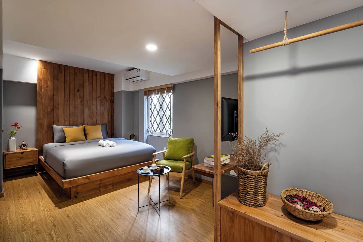 Een moderne slaapkamer met een houten bed, een groene stoel, een klein tafeltje en een televisie aan de muur.