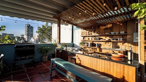 Eine Außenküche mit einer Holzpergola, einer eingebauten Bank und Kübelpflanzen.