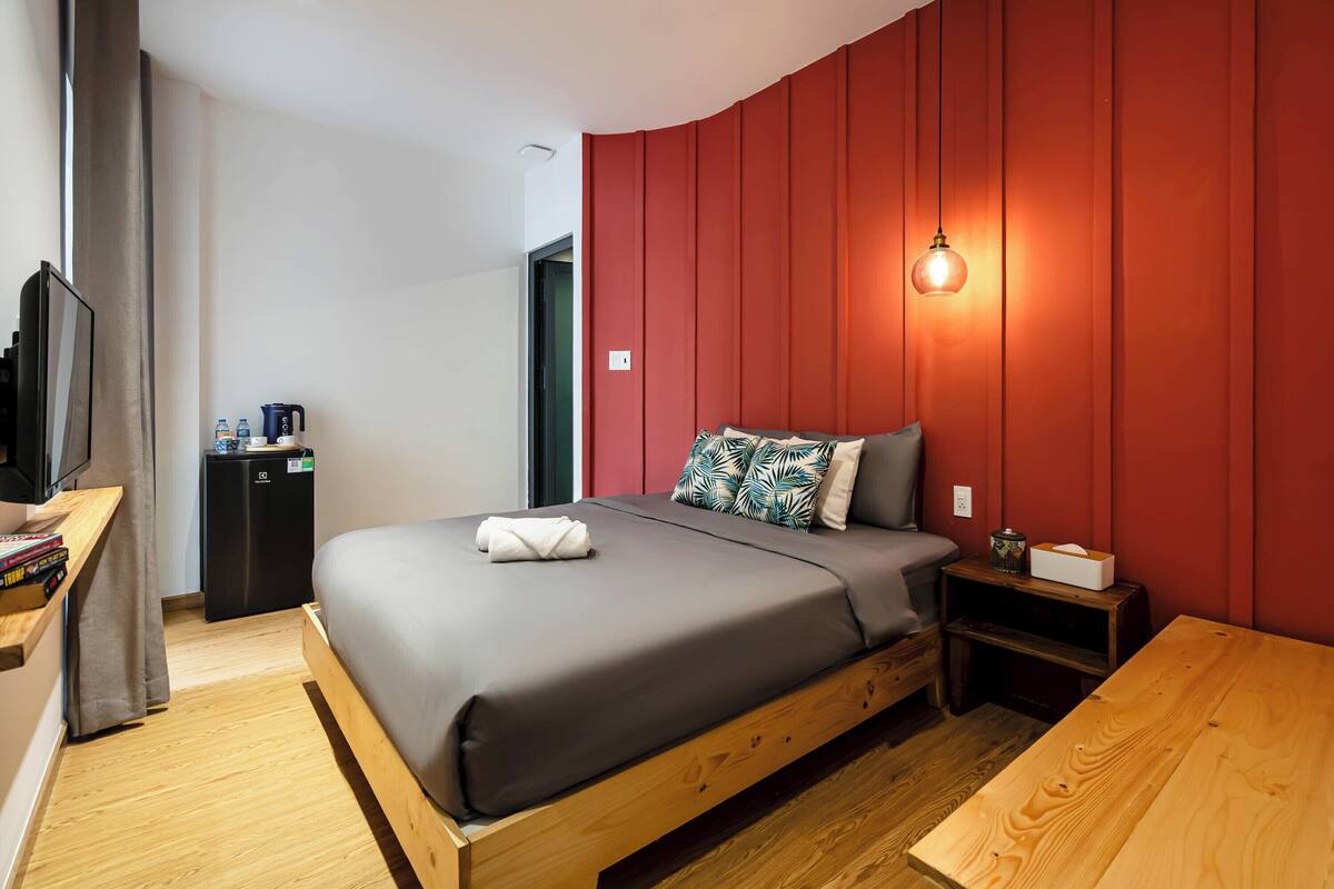 Een moderne slaapkamer met een houten bed, een televisie, een klein bureau en een rode accentmuur.