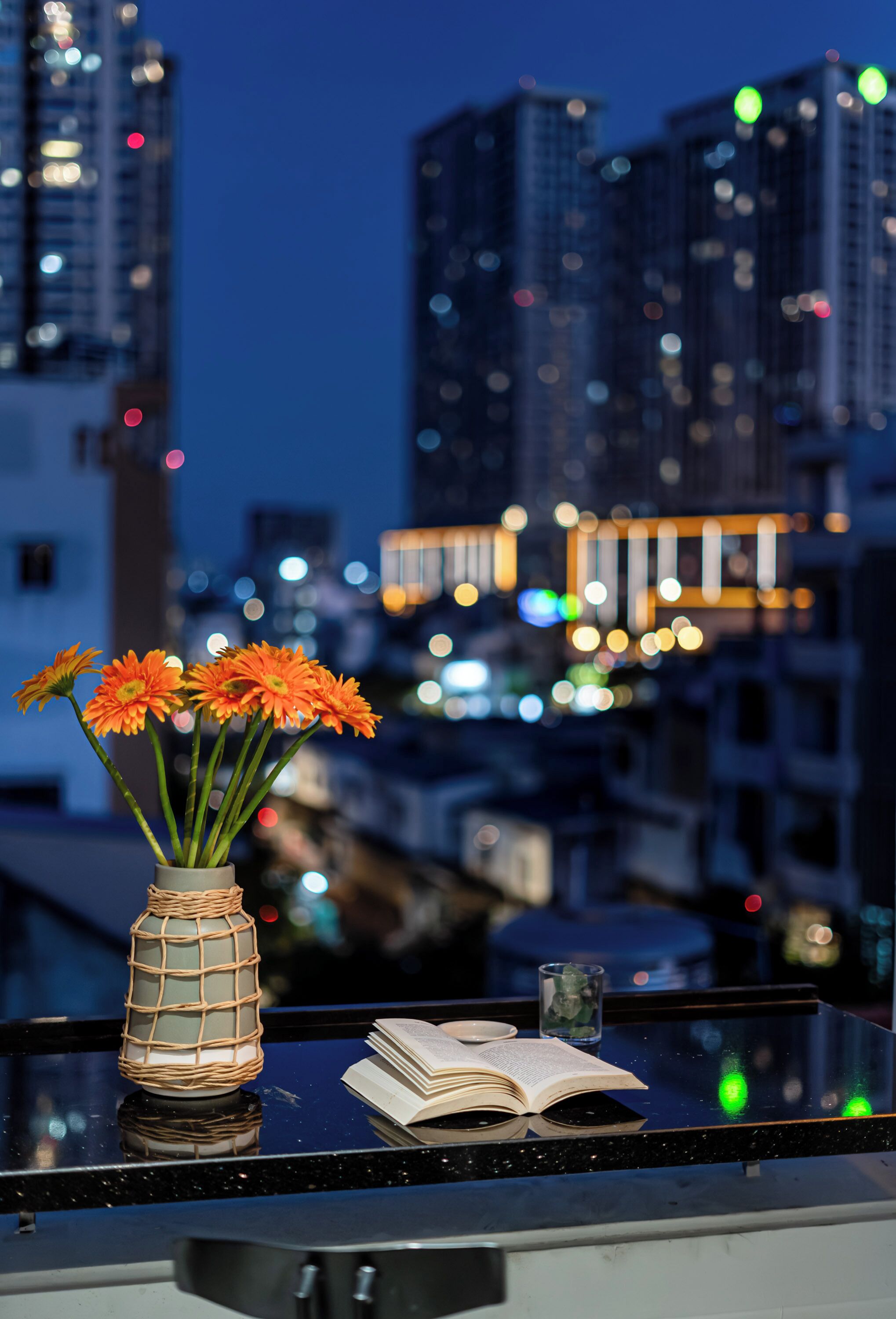 A cityscape at dusk with a table featuring a vase of flowers and an open book.