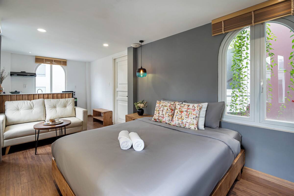 Een moderne hotelkamer met een groot bed, een bank, een kleine tafel en een keuken in de achtergrond.