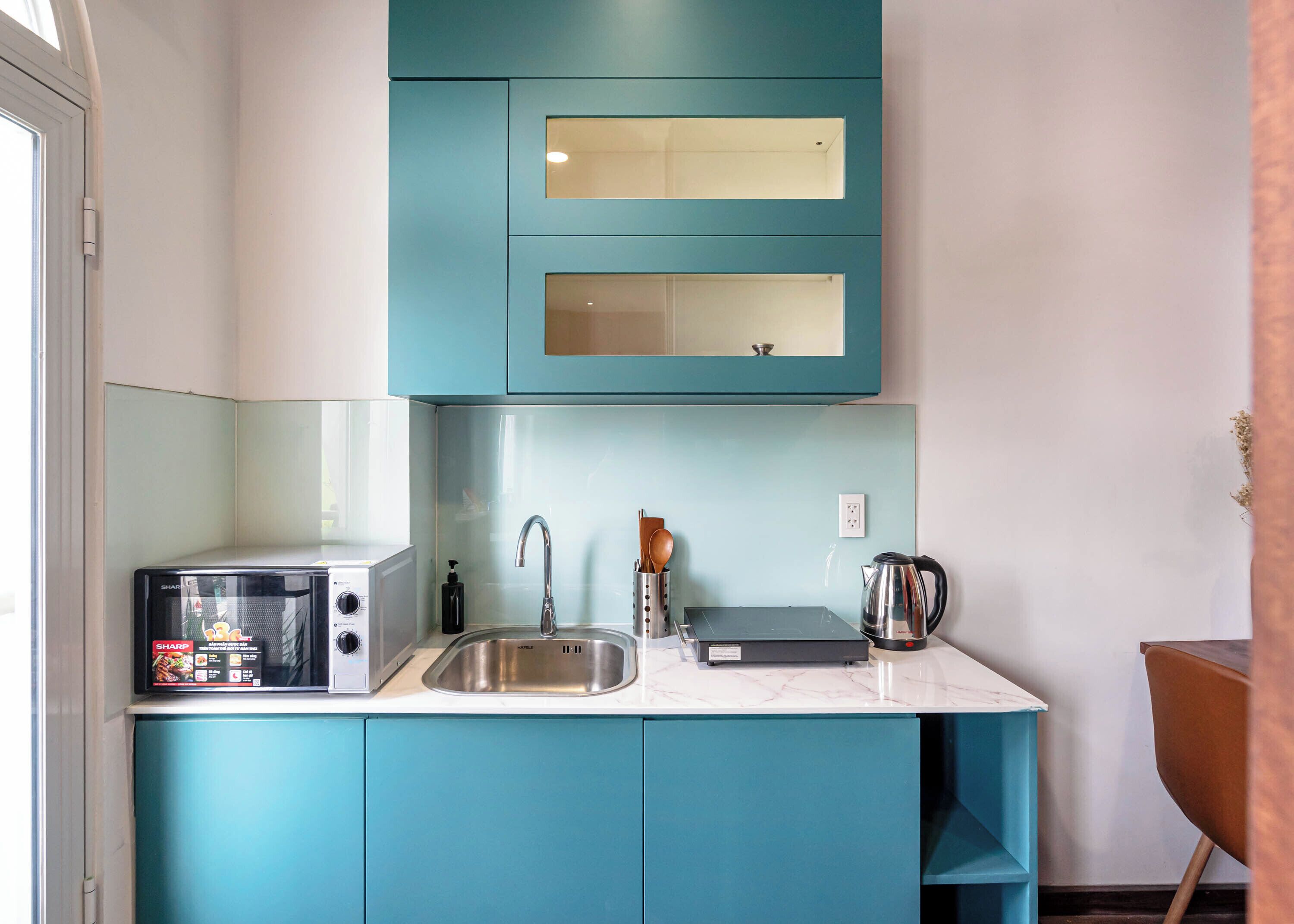 A compact kitchen with teal cabinetry, a stainless steel sink, a microwave, and a kettle.