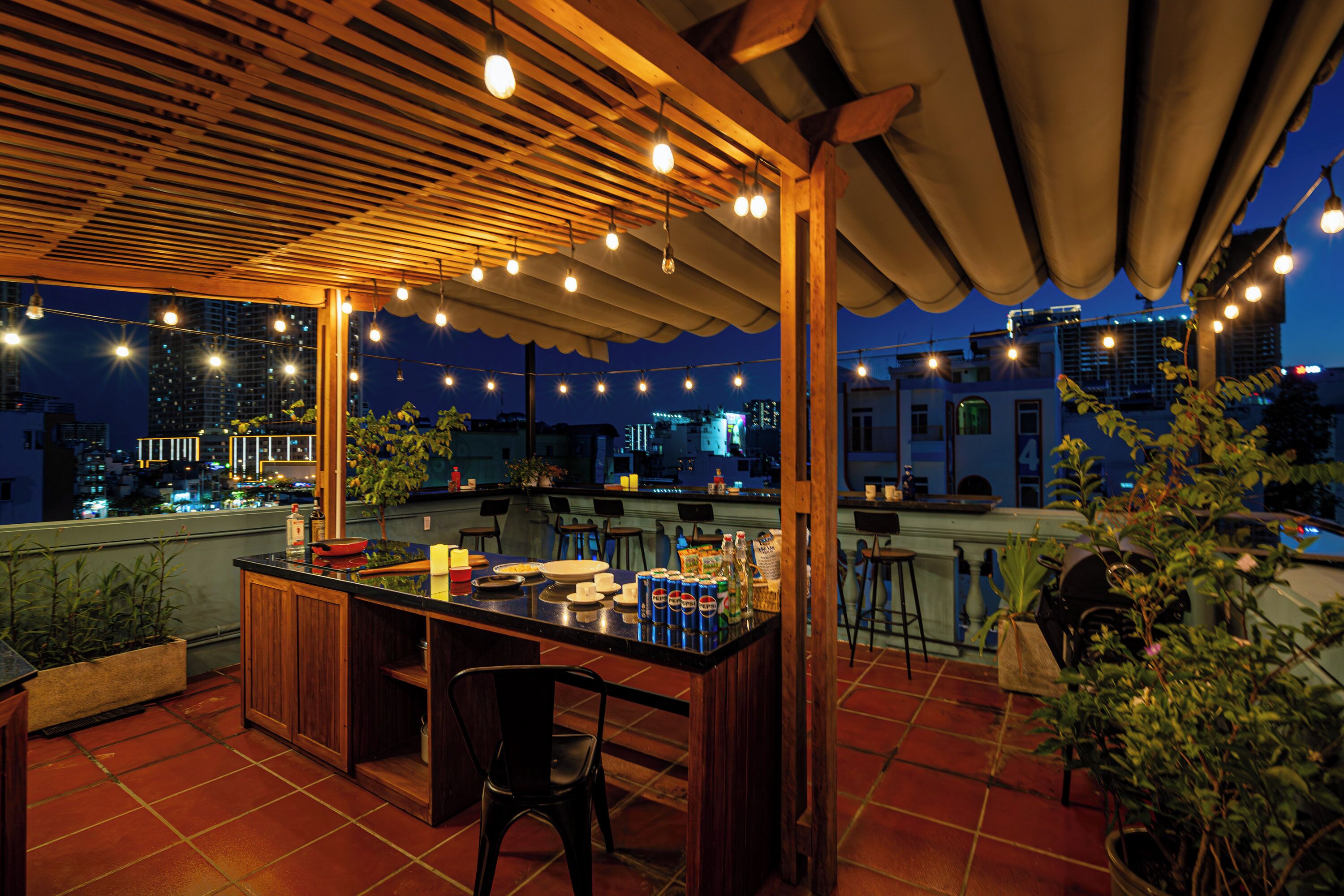 Een dakterras met een houten pergola, zitplaatsen buiten en uitzicht over de stad in de schemering.