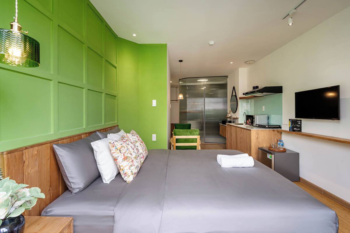 Een moderne hotelkamer met een groot bed, een groene accentmuur, een kitchenette en een flatscreen televisie.