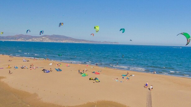 Una playa con gente, tiendas de campaña y cometas.
