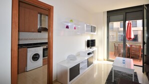 Un espacio habitable compacto con cocina, lavadora, televisor de pantalla plana y comedor con mesa y sillas.