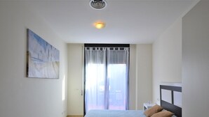 Un dormitorio con cama, ventana con cortinas, luz de techo y un cuadro en la pared.