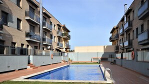 Una piscina rodeada de césped y un sendero de ladrillo, con edificios de varios pisos al fondo.