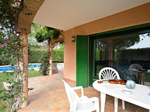 En udendørs terrasse med et bord og stole, en swimmingpool og udsigt til haven.