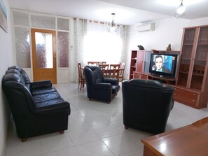 Un salon comprenant un canapé, un téléviseur et un coin repas avec des chaises et une table.