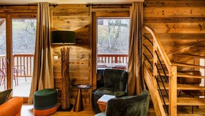 A cozy cabin interior with a wooden staircase, a seating area with a table and chairs, and a view of the outdoors through large windows. - Spacious 4-Bedroom Apartment with Wi-Fi and Garage in Les Gets (Les Gets)