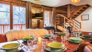A dining area with a wooden table set for a meal, a staircase, and a view of trees outside. - Spacious 4-Bedroom Apartment with Wi-Fi and Garage in Les Gets (Les Gets)