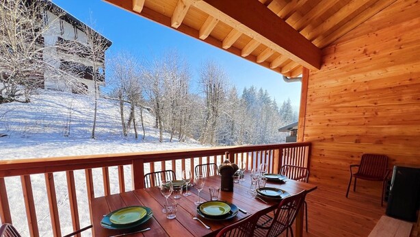A wooden deck with a table set for dining, overlooking a snowy landscape with trees. - Spacious 4-Bedroom Apartment with Wi-Fi and Garage in Les Gets (Les Gets)