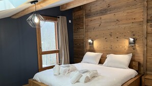 A bedroom with a wooden bed frame, a skylight, a window with curtains, and two wall-mounted lights. - Spacious 4-Bedroom Apartment with Wi-Fi and Garage in Les Gets (Les Gets)