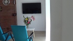 Una sala de estar moderna con una pared de ladrillo, un televisor de pantalla plana montado sobre una pequeña mesa redonda y dos sillas azules.