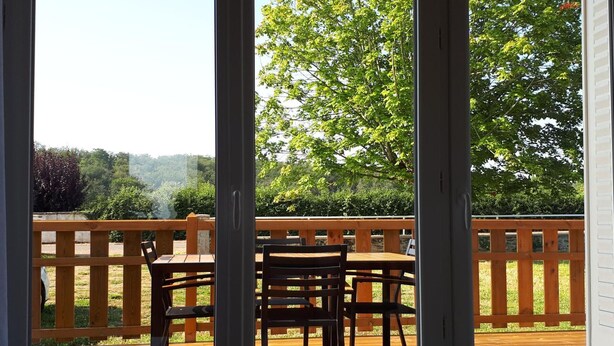 Terraza de madera con una mesa y sillas, rodeada por una valla de madera, con vistas a un paisaje verde.