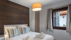 A neatly made bed with white linens and striped pillows, a wooden headboard, a hanging lamp, and a window with curtains. - Bright apartment near slopes with parking, pets allowed (Megève)