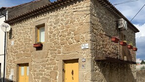 A stone building with a yellow door, a small window, and a balcony with potted plants. - House in granite stone with a century old in center Portugal. Open Space. (Tinalhas)
