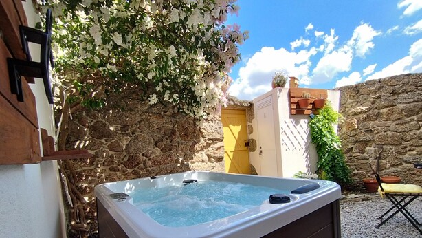 A hot tub in a stone-walled outdoor area with a wooden deck, a yellow door, and a cactus plant. - House in granite stone with a century old in center Portugal. Open Space. (Tinalhas)