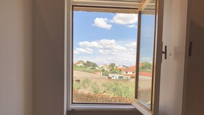 A room with a wooden floor, a window with an open door, and a vase on the floor. - House in granite stone with a century old in center Portugal. Open Space. (Tinalhas)