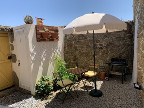 A patio with a table and chairs, a white umbrella, a grill, and a stone wall.