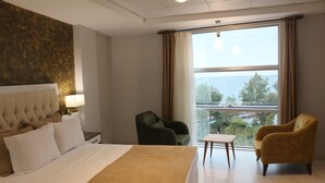 A hotel room with a bed, a chair, a small table, and a large window offering a view. - ALARGA PREMIER (Trabzon)