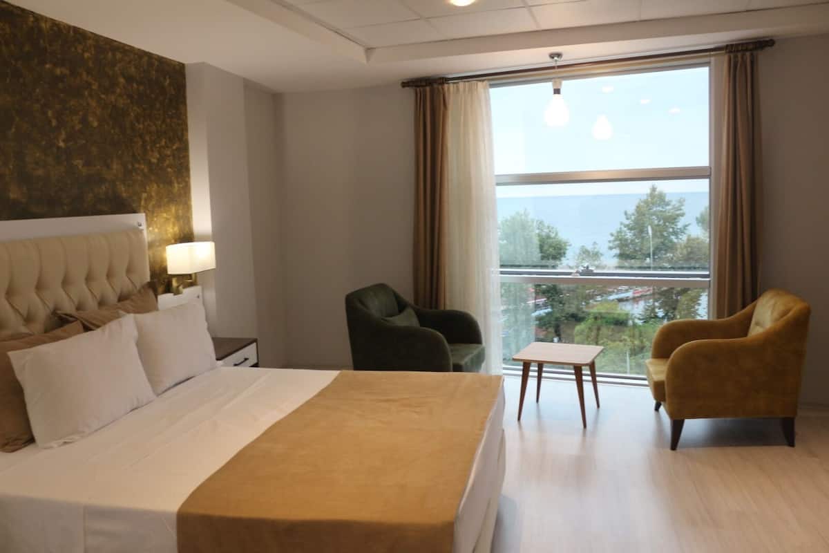 A hotel room with a bed, a chair, a small table, and a large window offering a view.