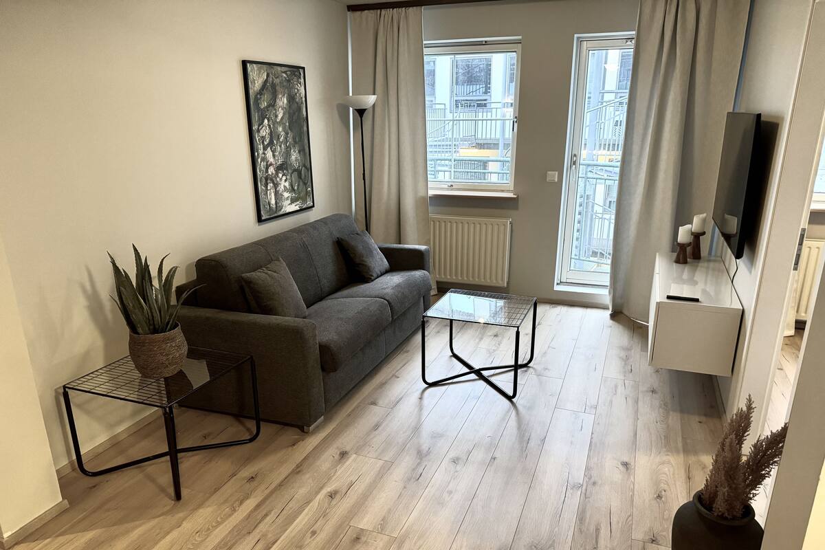 A modern living room with a grey sofa, a small coffee table, a floor lamp, and a potted plant.