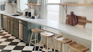 Een moderne keuken met een zwart-wit betegelde vloer, een bar met barkrukken, een spoelbak en een koffieapparaat.