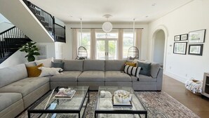 Een moderne woonkamer met een grijze modulaire bank, twee glazen salontafels en een trap met zwarte leuningen.