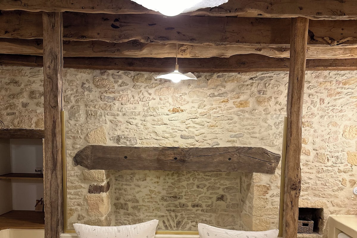 A rustic room with exposed wooden beams, a stone wall, and a bed with white pillows and a green bedspread.