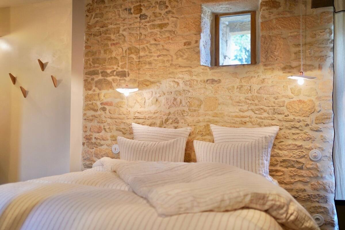 A bedroom with a stone wall, a small window, and a bed with striped bedding.