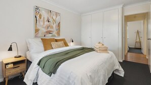 Et hotelværelse med en seng, et natbord, en lampe, et maleri og et klædeskab.