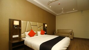 A hotel room with a large bed, a nightstand, a sofa, and a ceiling fan. - Sindhura Grand (Hyderabad)