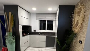 Eine moderne Küche mit weißen Schränken, einem Marmorboden und einem großen Fenster.