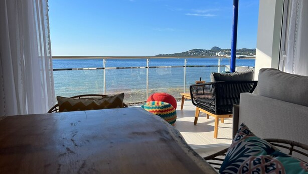 Ein Balkon mit Meerblick, eine Couch, ein Sessel und ein farbenfroher Hocker.