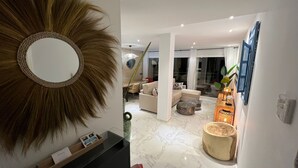 Un salon moderne avec un grand miroir, un canapé et une table basse. On aperçoit à l’arrière-plan un coin repas avec une table et des chaises.