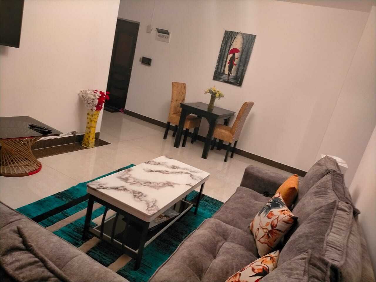 A modern living room with a grey sofa, a marble coffee table, and a dining area with a table and chairs.