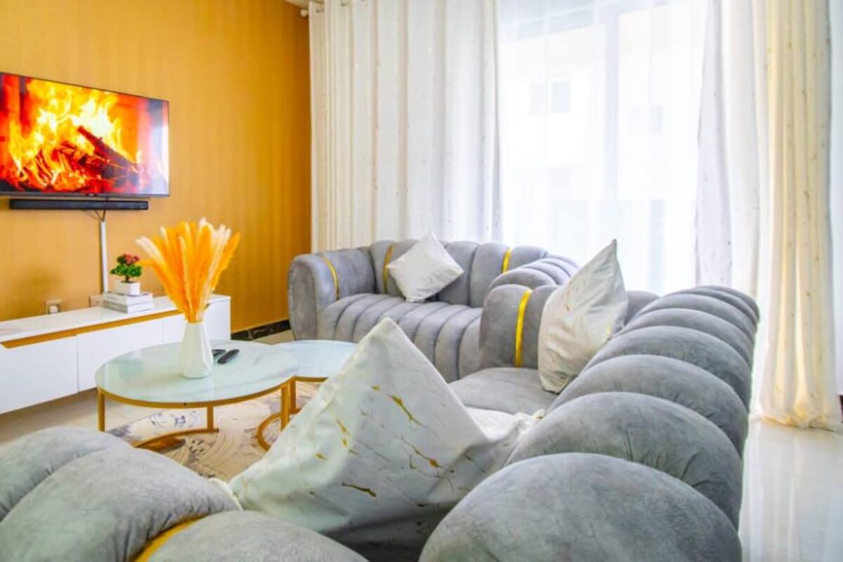 A living room with a sofa set, a coffee table, a TV mounted on the wall, and a vase with flowers on a side table.