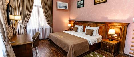 Habitación de hotel con una cama de madera, un escritorio, una silla, una mesita de noche con lámpara y una alfombra verde estampada.
