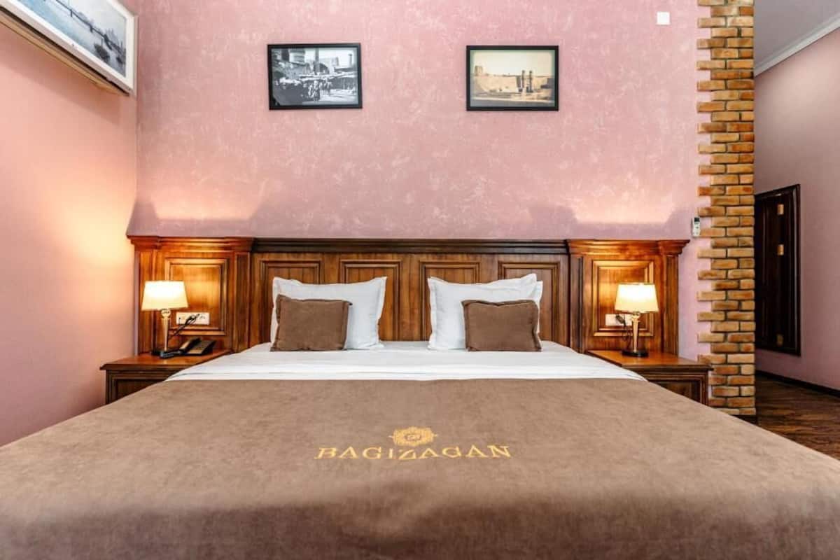 Ett hotellrum med en stor säng, två sängbord med lampor, en vägg med synliga tegelstenar och två inramade tavlor på väggen.